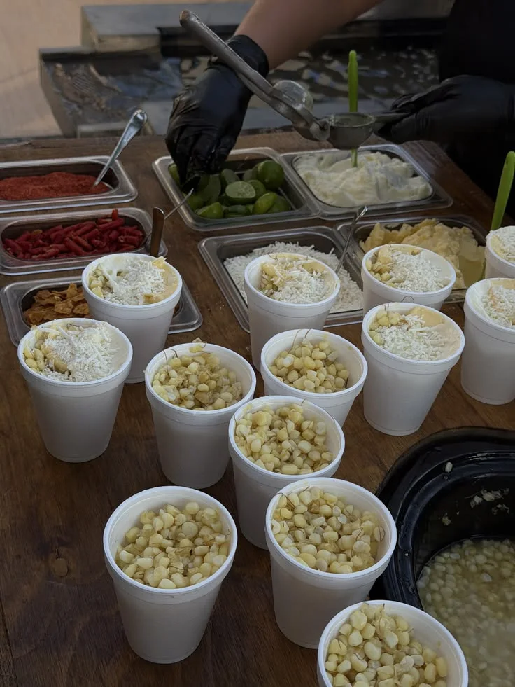 Vasos de esquites servidos junto a una barra de ingredientes